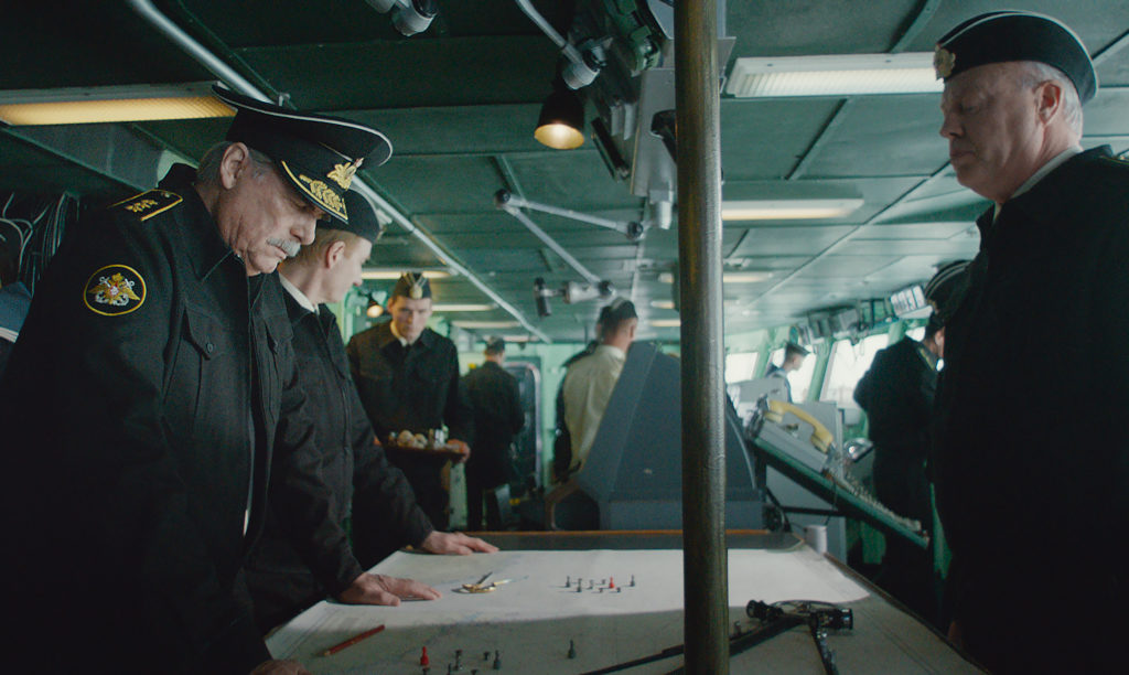 Marineoffiziere stehen um einen Kartentisch auf der Brücke eines Schiffes herum, links ein Admiral.