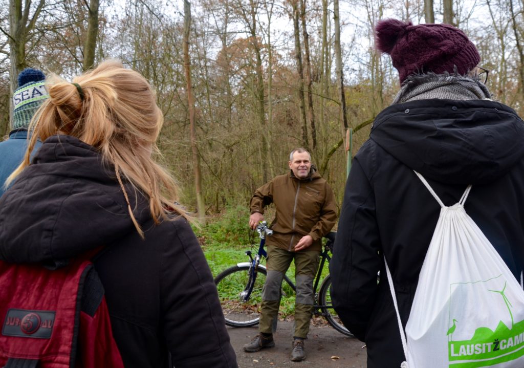 Das Bild zeigt den Revierförster Thomas Knorr. Er steht vor einer Gruppe von Studierenden auf einem Waldweg und ist auf sein Fahrrad gelehnt.