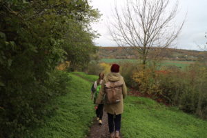 Zwei Wandererinnen auf einem schmalen Pfad mit Ausblick auf weite, grüne Hügel