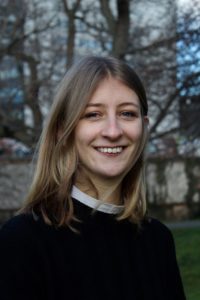 Das Foto zeigt die Kolumnistin Lisa in Nahaufnahme. Sie steht auf einer Wiese und trägt einen schwarzen Pullover. Sie lächelt in die Kamera. 