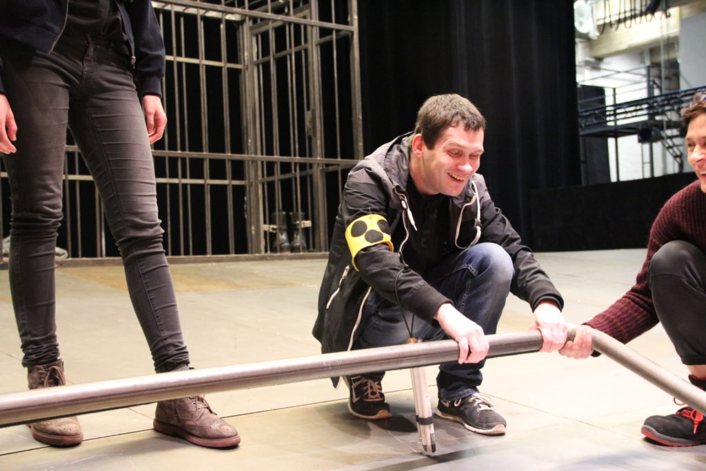 Dennis ertastet knieend die Eisenstange, die die Bühne zum Publikum hin abgrenzt.