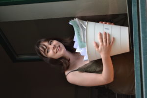 Kolumnistin Sophie mit einem Mülleimer in der Hand schaut aus dem geöffneten Fenster