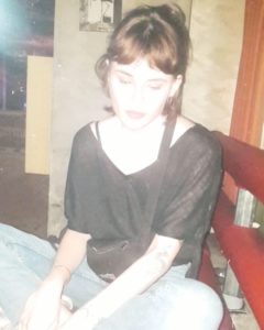 Junge Frau sitzt auf Fensterbank in dunklem Raum.