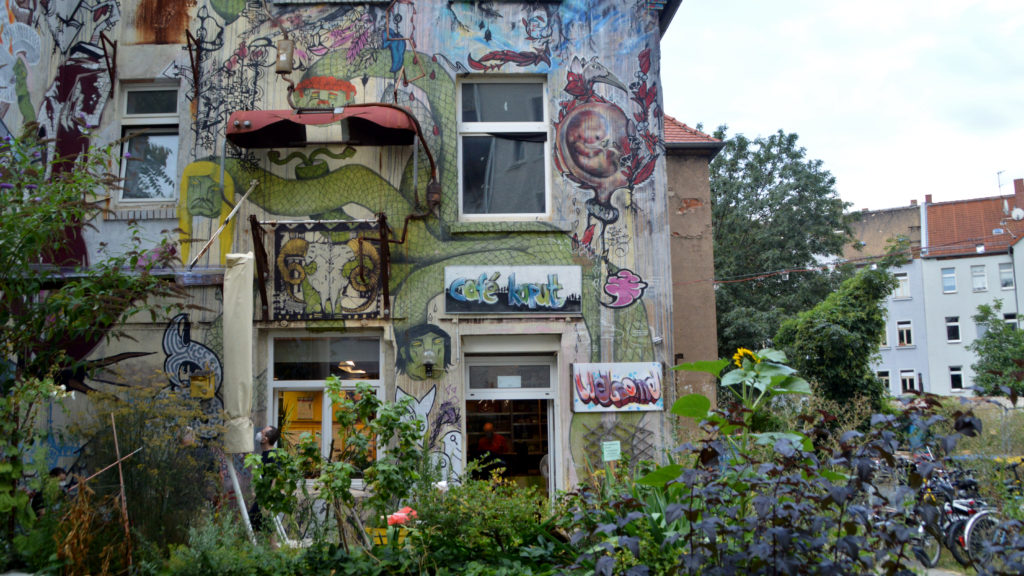 Eine Hauswand mit allerlei Graffitis. Es ist eine vierköpfige Schlange und ein Willkommensschild zu sehen.