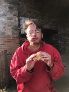 Laurenz hat einen roten Pulli an und isst genussvoll ein Brötchen.