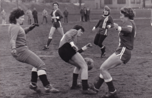 Schwarzweiß Bild zeigt zwei Fußball Spielerinnen im Zweikampf um den Ball. 