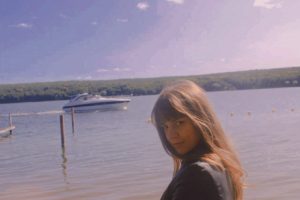 Kolumnistin Theresa steht an einem See mit Boot im Hintergrund und schaut in die Kamera.