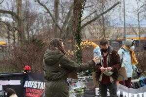 Ein Mensch wirft den Inhalt einer Erdnussflipstüte durch die Luft auf dem kleinen Wilhelm-Leuschner_platz.