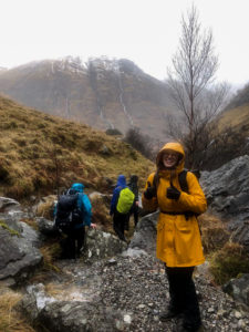 Die Autorin Julie-Madeline Simon steht in einer gelben Wanderjacke vor einem Berg. Hinter ihr sind weitere Wandernde zu sehen.