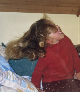 Ein weibliches Kind im Kindergartenalter im roten Pulli tollt auf einem Bett herum.