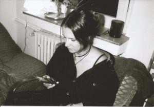 Annika sitzt in einem Raum auf einer Couch und schaut auf ihr Handy. Das Foto ist schwarzweiß.