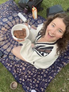Kolumnistin Johanna sitzt auf einer Picknickdecke, hält eine Schale mit Bananenbrot in den Händen und grinst in die Kamera. 