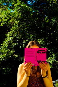 luhze-Autorin Johanna mit dem neonpinken Sachbuch "Who cares!" von Mirna Funk draußen in der Sommersonne