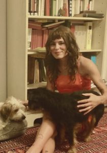 Kolumnistin Sara sitzt auf einem Teppich vor einem Bücherregal und streichelt zwei Hunde.