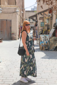 Kolumnistin Natalie im Urlaub, sie trägt ein langes Kleid und eine Sonnenbrille und lächelt in die Kamera, hinter ihr sind Häuser zu erkennen