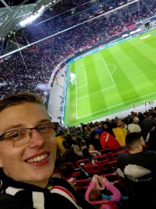 Kolumnist Eric bei einem Fußballspiel im Stadion, im Hintergrund Menschenmassen und das Spielfeld, auf dem gerade Fußball gespielt wird