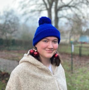Kolumnistin Clara lächelt in die Kamera, auf dem Kopf trägt sie eine blaue Pudelmütze