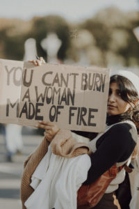 Arezoo mit einem Schild in der Hand, das die Aufschrift trägt "You can't burn a woman made of fire"