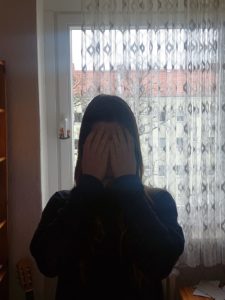 Kolumnistin Isabella steht vor einem Fenster und versteckt ihr Gesicht hinter ihren Händen