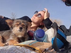 Kolumnistin Annika liegt auf einer Picknickdecke und sonnt sich, neben ihr liegt ein kleiner Hund