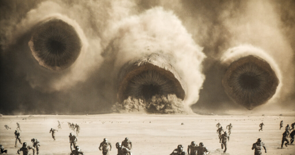 Man sieht drei Sandwürmer aus dem Dune Universum. Im Vordergrund flüchten Menschen.